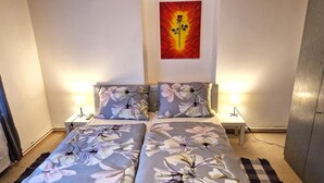 Een tweepersoonsbed met bloemenbeddengoed, twee bedlampjes, een nachtkastje en een aan de muur hangend kunstwerk.