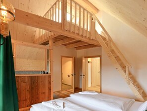 Un interior de madera con una escalera que conduce a un nivel superior, una cama con ropa de cama blanca y un mueble de pared de madera.