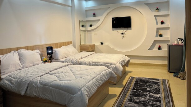 A modern bedroom with two beds, a flat-screen TV mounted on the wall, and a decorative rug. - Farido Pyramids (Giza)