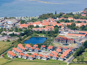 Luchtbeeld van een kustgebied met woonhuizen met rode daken, een klein meer en een kerktoren.