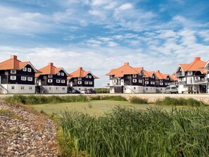 Uma fileira de casas modernas, com dois andares, telhados vermelhos e varandas, localizada ao lado de uma área gramada.