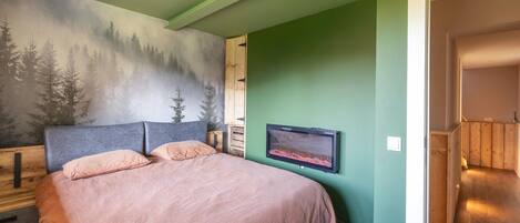 A bedroom with a bed, a wall-mounted TV, and a forest mural.