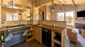 Une cuisine rustique avec des meubles en bois, une cuisinière à gaz, un lave-vaisselle et une grande fenêtre qui laisse entrer la lumière naturelle.