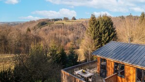 Une cabane en bois dotée d’une terrasse et offrant une vue sur une vallée boisée.