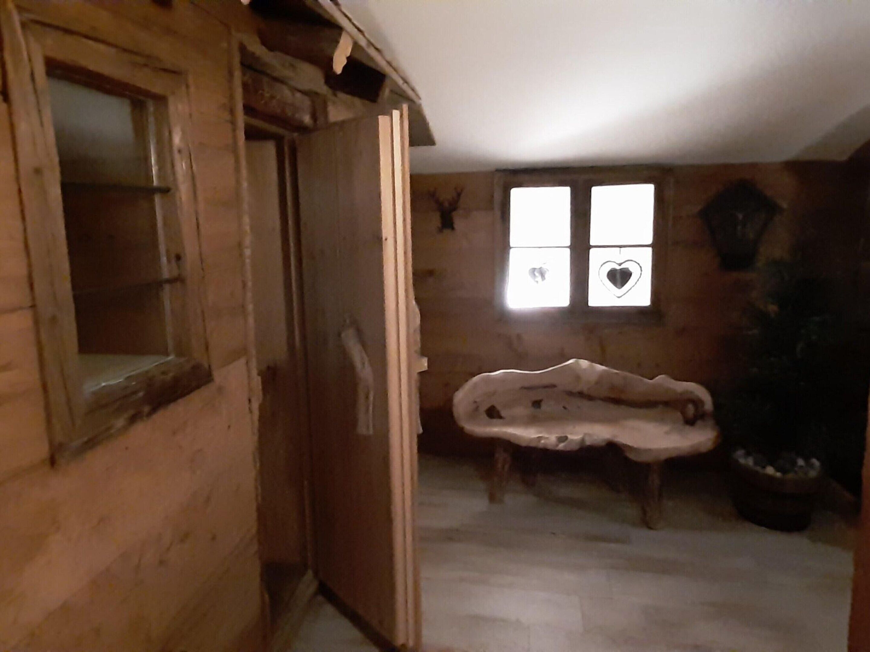 Ein rustikales Holzzimmer mit einer großen Badewanne, einer Holztür und einem Fenster mit dekorativen Schnitzereien.