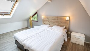 Ein Schlafzimmer mit schrägem Dach, einem Oberlicht, einem Bett mit weißer Bettwäsche, einem Holzkopfende und einem Nachttisch mit Lampe.
