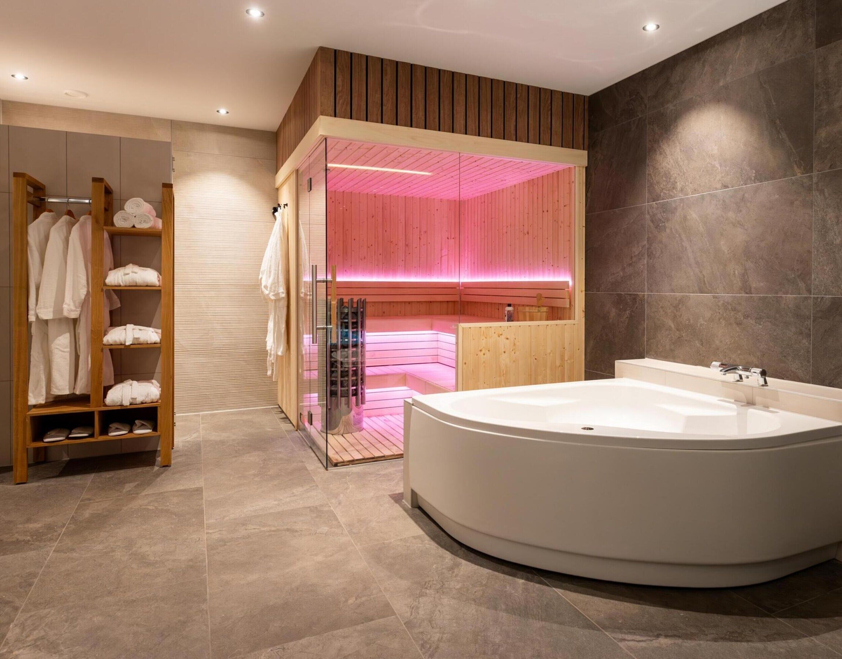 A modern bathroom with a freestanding bathtub, a wooden vanity, and a glass shower enclosure with pink lighting.