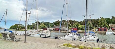 A marina with several sailboats docked, a wooden walkway, and buildings in the background.