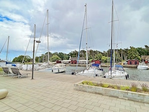 Un port de plaisance où sont amarrés plusieurs voiliers, une promenade en bois et des bâtiments en arrière-plan.