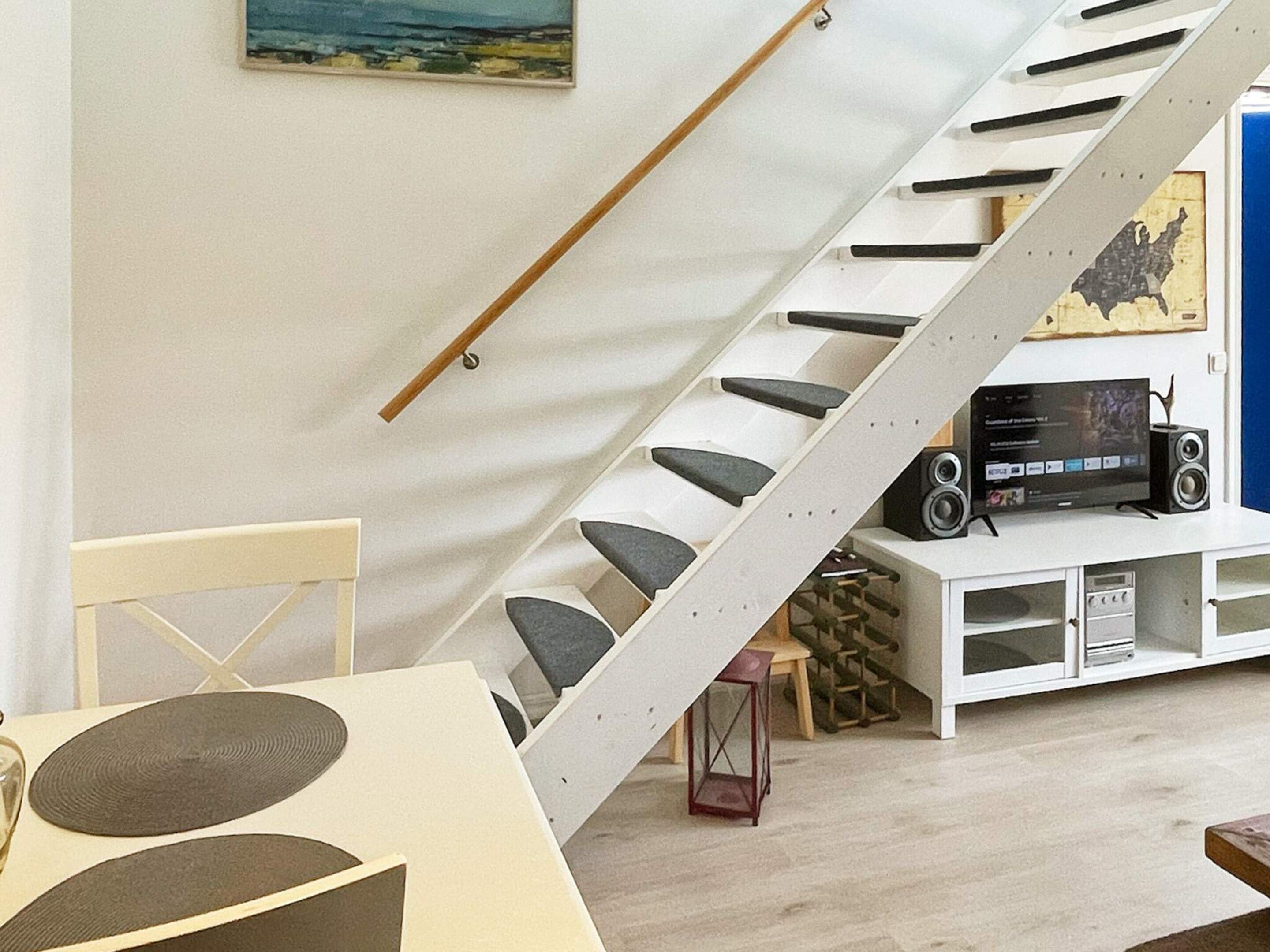 A modern interior with a staircase, a flat-screen TV, speakers, and a painting on the wall.