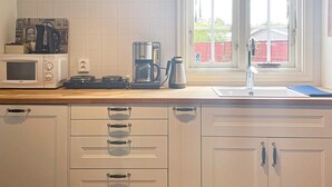 A kitchen with a microwave, coffee maker, and kettle on the counter, a window with a view of a red building, and a sink with a faucet. - 4 Star Holiday Home in Ahus (Aahus)