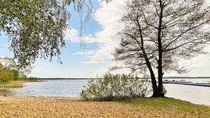 A lakeside view with a sandy beach, trees, and boats in the distance. - 4 Star Holiday Home in Ahus (Aahus)
