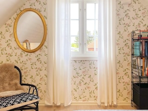 A room with a window, a mirror, a chair, a bookshelf, and floral wallpaper. - 4 Star Holiday Home in Ahus (Aahus)