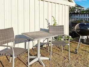 An outdoor patio with a table and four chairs, a barbecue grill, and a white fence in the background. - 4 Star Holiday Home in Ahus (Aahus)