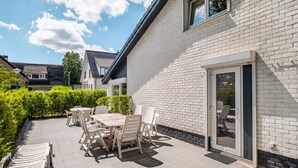 Eine Terrasse mit Gartenmöbeln, einer weißen Ziegelwand und einer Schiebetür.