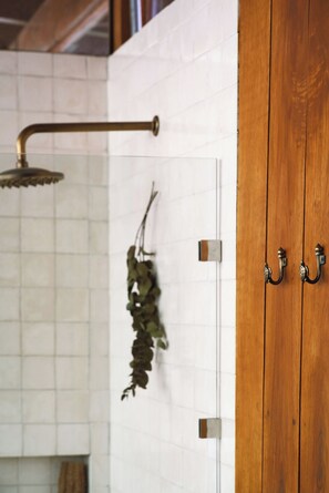 Un baño con pared de azulejos blancos, puerta de madera y ducha con cabezal curvo.