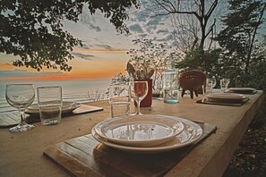 Mesa lista para una comida con vista al océano y al atardecer.