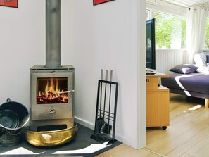 A modern living room with a wood-burning stove, a sofa, a television, and a window with a view of greenery.