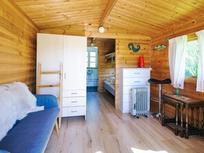 A wooden cabin interior with a bed, a desk, a radiator, and a window with curtains.