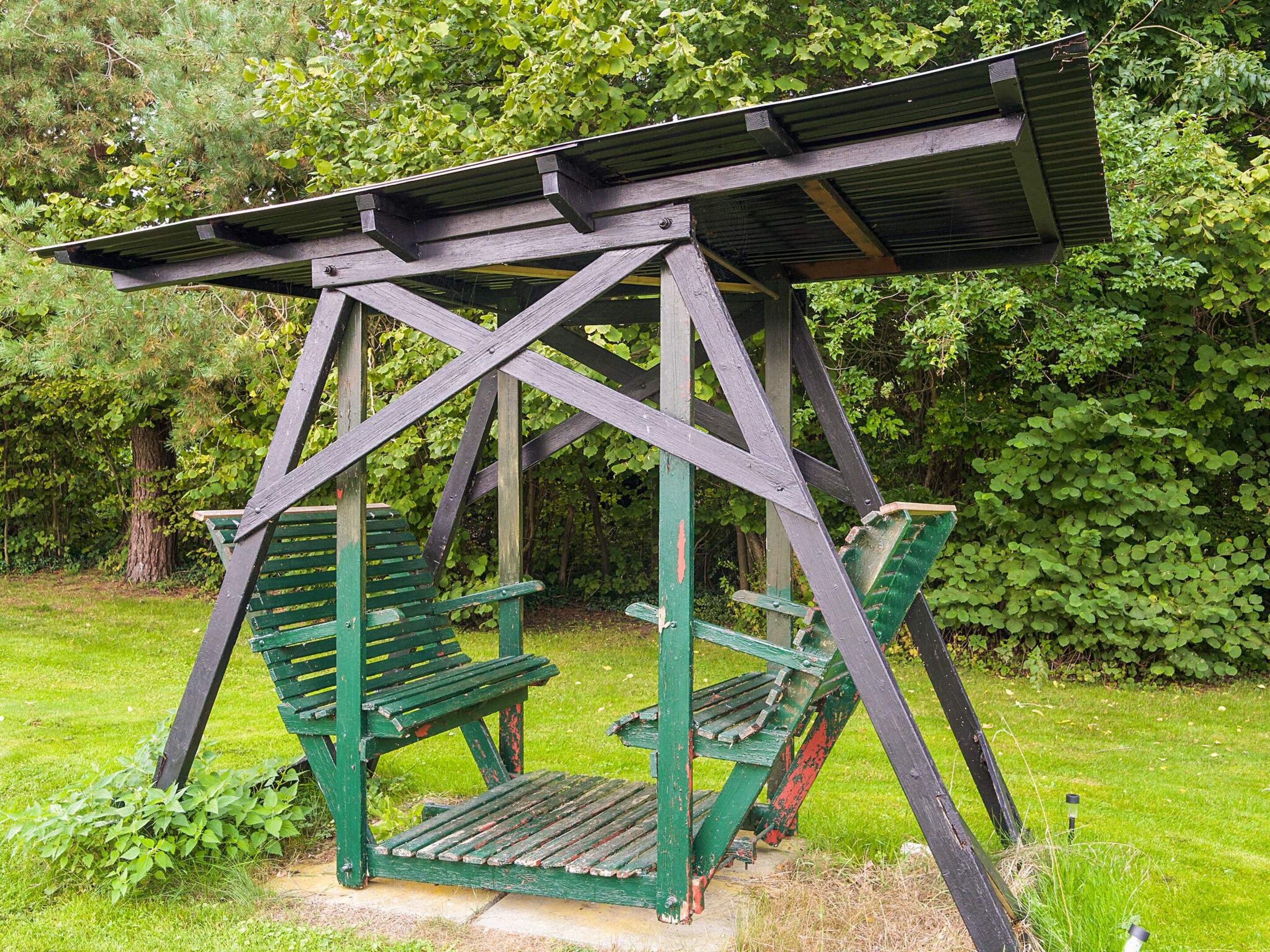 A wooden swing structure with benches, surrounded by greenery.