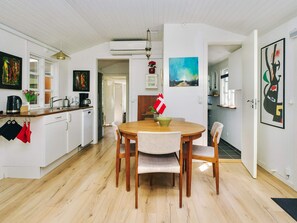 A modern kitchen with white cabinets, a wooden dining table, and a flag on the wall. - 8 Person Holiday Home in Holbaek (Holbaek)