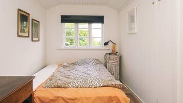 Un dormitorio con cama, escritorio, ventana con vistas y lámpara en una cómoda.