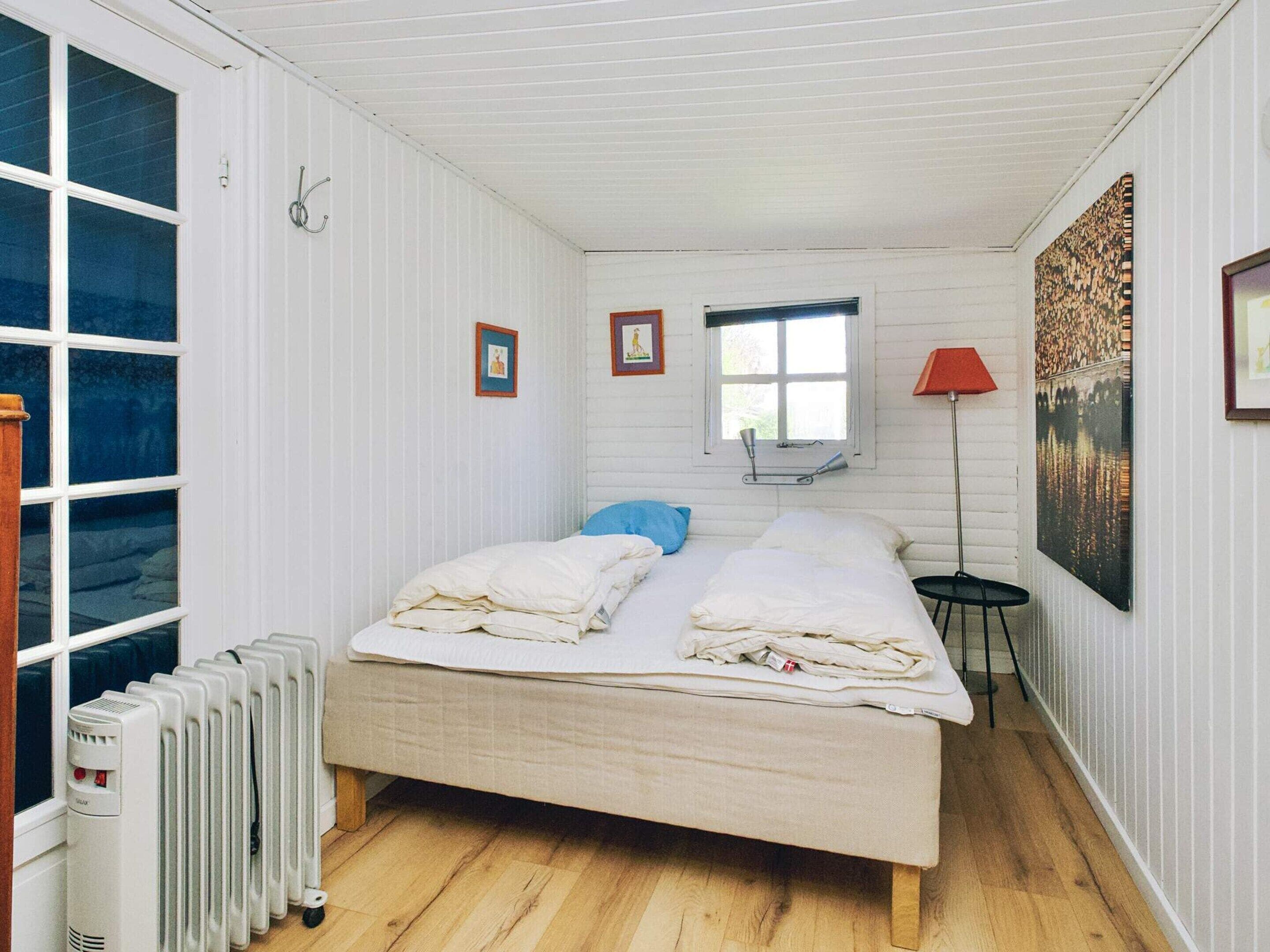 Een kamer met een bed, een radiator, een raam, een lamp en een schilderij.
