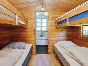 Una cabaña con dos literas, un baño pequeño con lavamanos y una puerta que da al exterior.