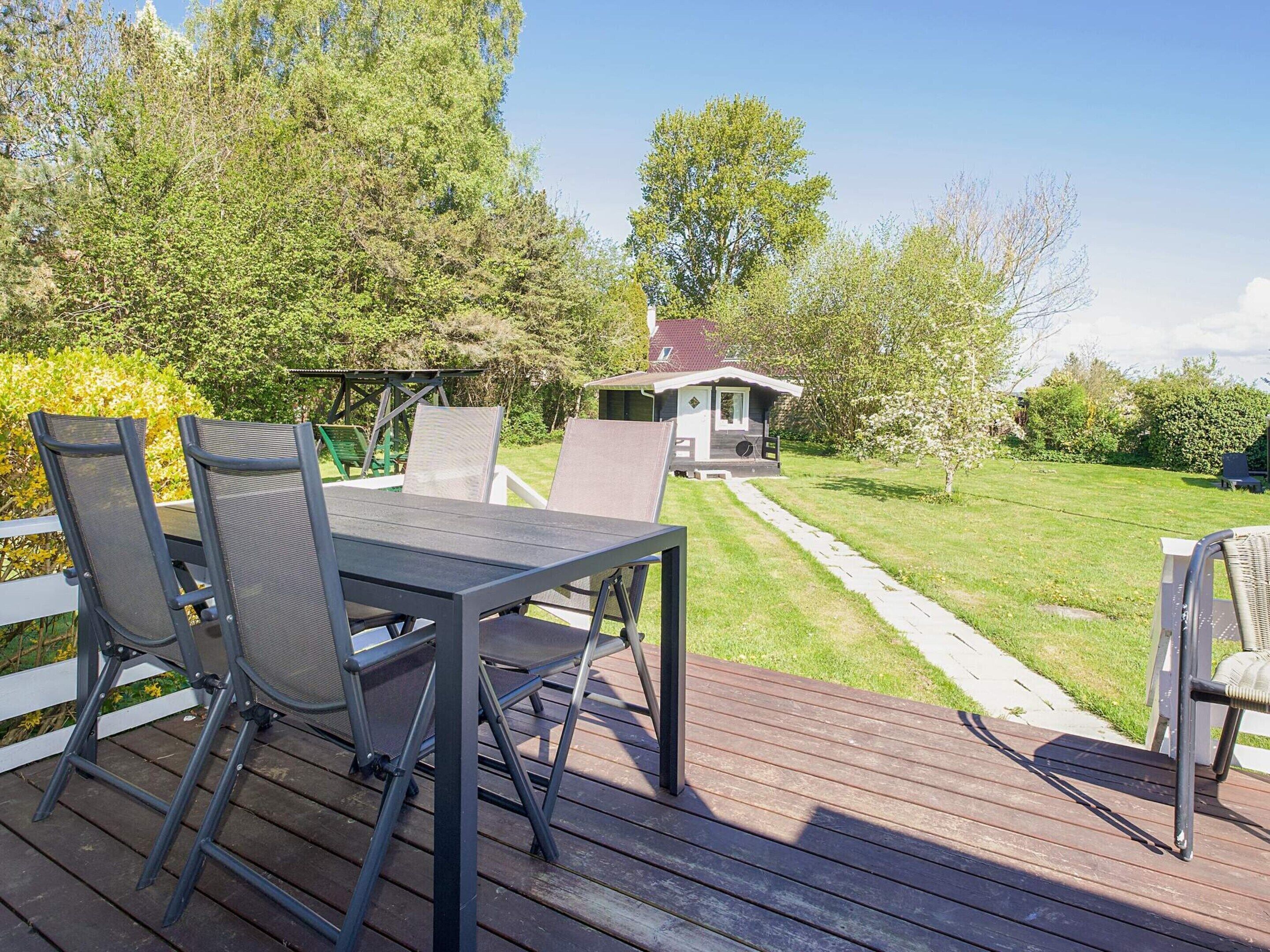 Une terrasse avec une table et des chaises, un chemin menant à une maison, et de la verdure tout autour.