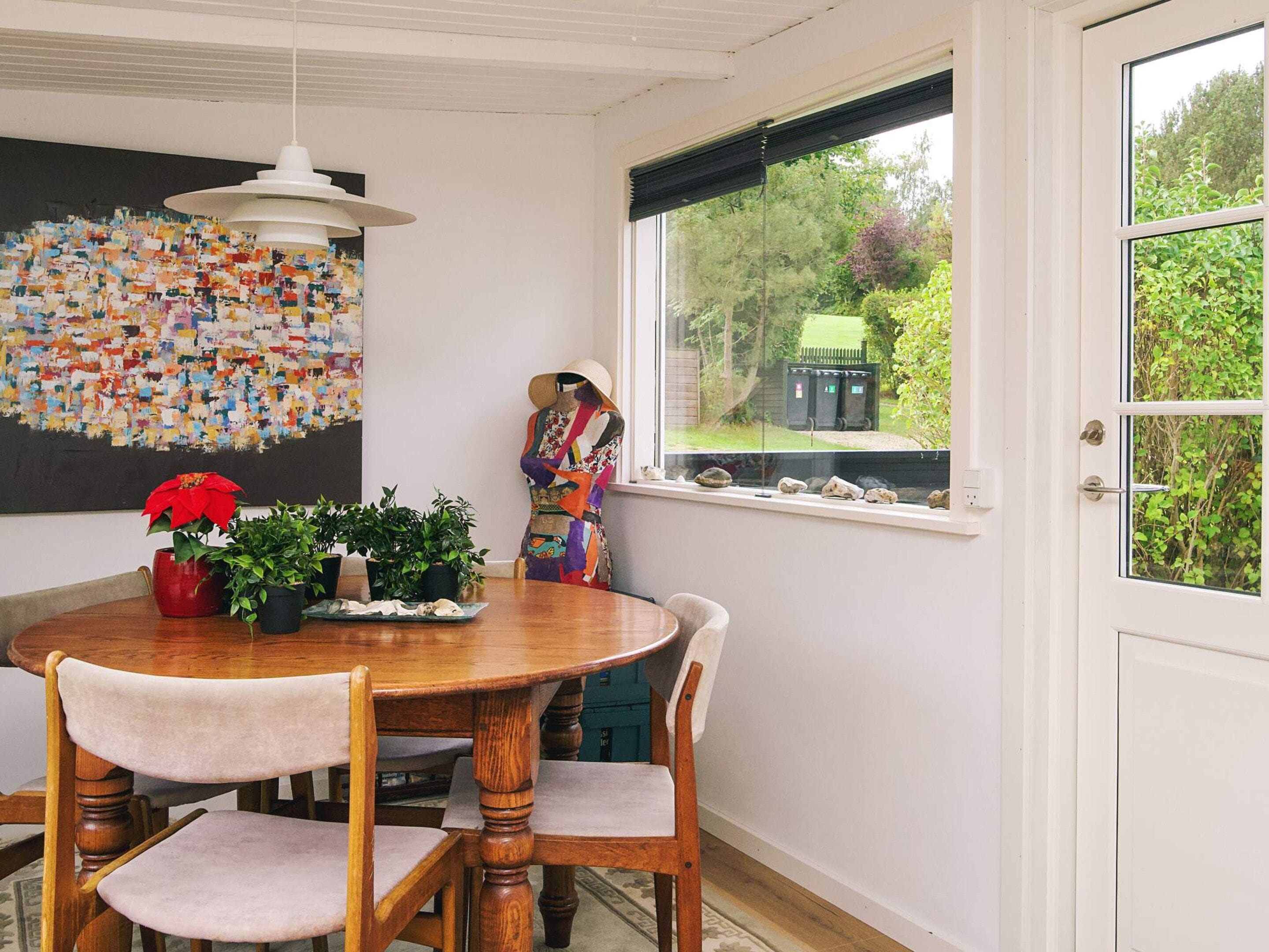 Un comedor con mesa de madera, sillas, lámpara colgante y vista al exterior a través de una ventana.