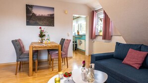 A cozy living room with a blue sofa, a dining table with chairs, and a kitchen in the background. - Heidetraum in der Pension Heidetraum (Bispingen)