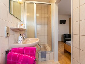 A bathroom with a sink, mirror, and shower. There is a bed and a TV in the adjacent room. - Heidetraum in der Pension Heidetraum (Bispingen)
