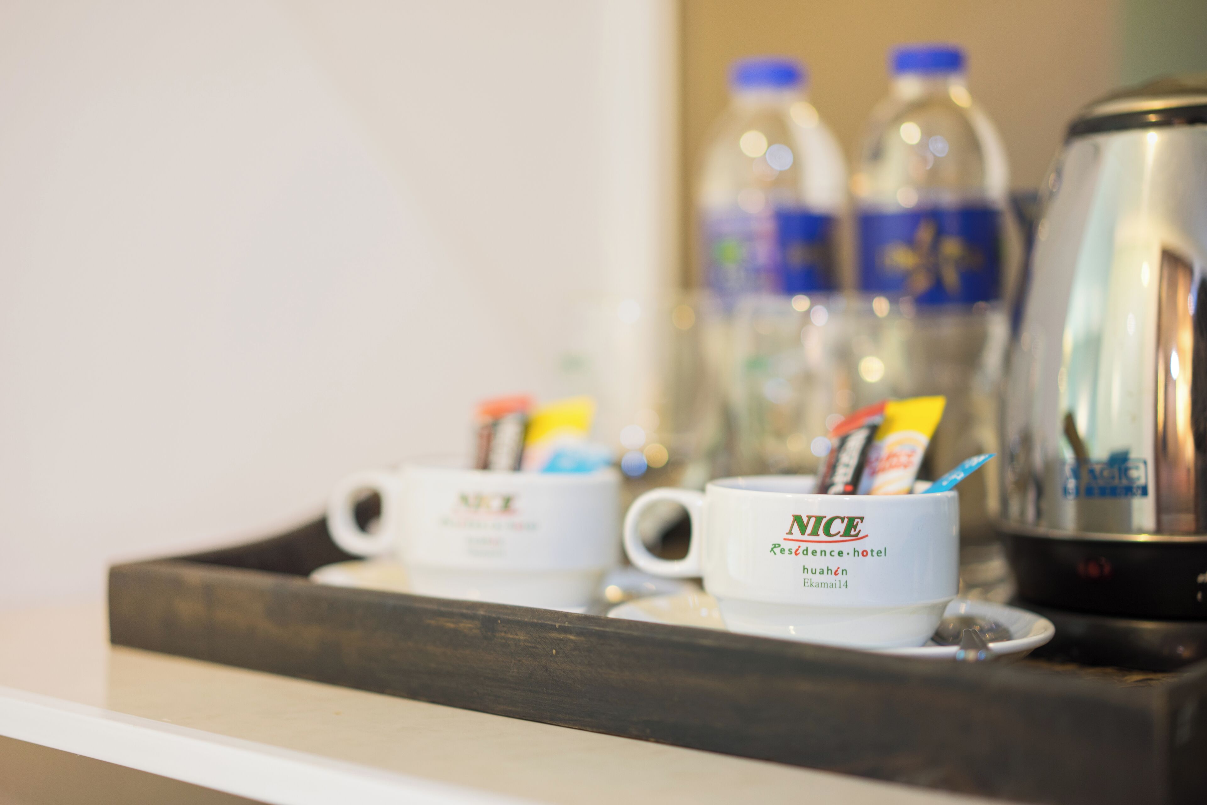 Een dienblad met twee mokken met de tekst 'NICE' en een koffiepot, plus twee waterflessen.
