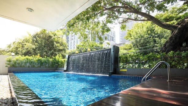 A swimming pool with a waterfall feature, surrounded by greenery and a wooden deck. - Nice Residence Bangkok Sukhumvit (Bangkok)