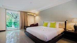 A hotel room with a large bed, a desk, a chair, a lamp, and a view of greenery through the window. - Nice Residence Bangkok Sukhumvit (Bangkok)