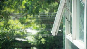 A window with a white frame, partially open, overlooking a blurred green landscape. - Nice Residence Bangkok Sukhumvit (Bangkok)