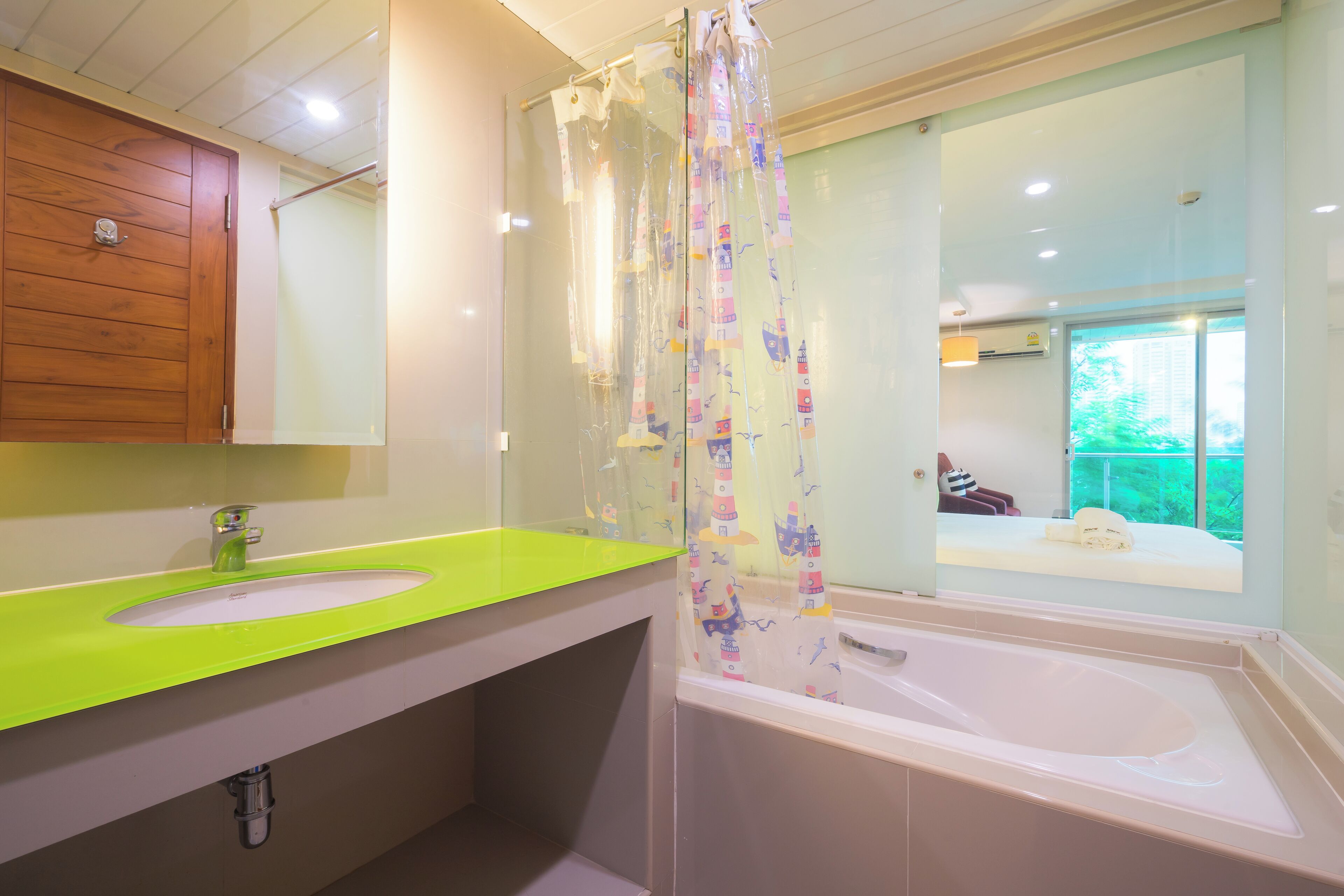 A bathroom with a green sink, a white bathtub, and a shower curtain with a nautical theme.