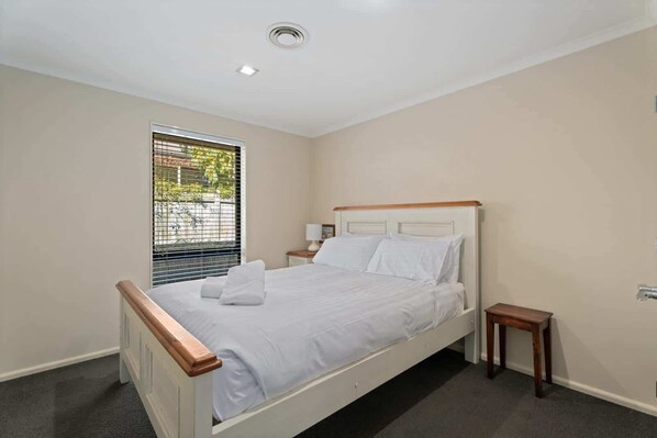 A bedroom with a bed, a bedside table, a window with blinds, and a ceiling light. - Mountain View Retreat Near Wanaka Township (Wanaka)