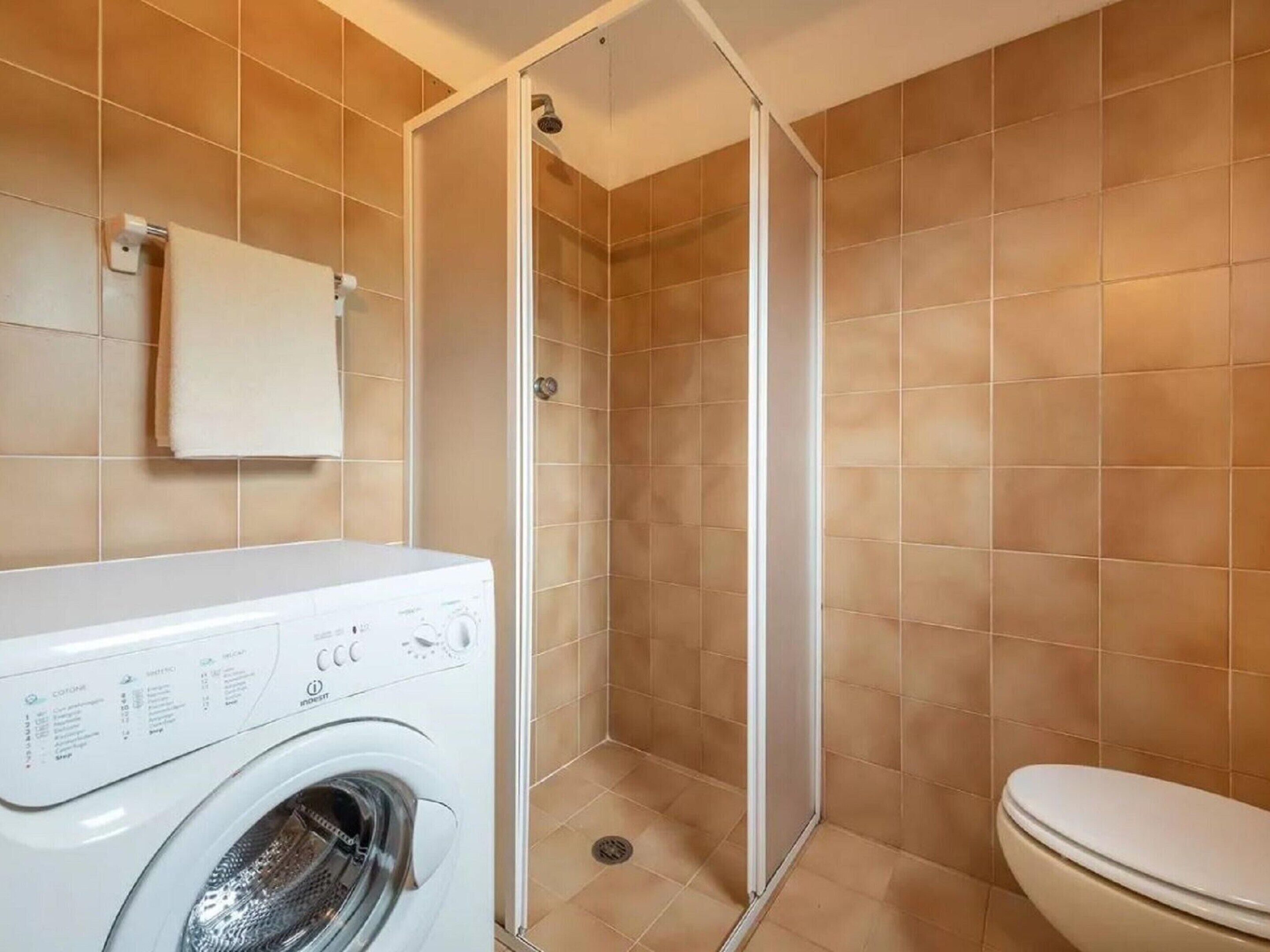 A compact bathroom with a washing machine, a toilet, and a shower enclosure.
