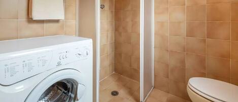 A compact bathroom with a washing machine, a toilet, and a shower enclosure.