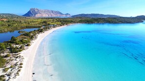 A coastal landscape with a clear blue sea, sandy beach, and a mountain in the background. - Pittulongu Villa Near Rocce Beach for 4 (Olbia)