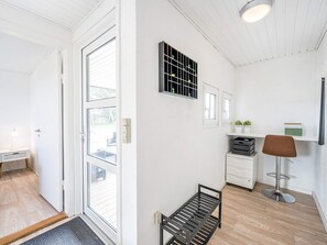 A modern interior with a white door, a bench, a small table with a lamp, a wall-mounted shelf with plants, and a chair. - 4 Star Holiday Home in Blavand (Blavand)