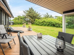 An outdoor patio with a wooden deck, wicker furniture, and potted plants. - 4 Star Holiday Home in Blavand (Blavand)