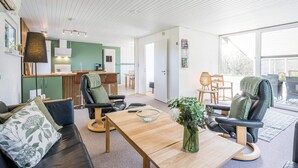 A modern living room with a sofa, chairs, a coffee table, and a kitchen area in the background.
