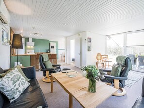 A modern living room with a sofa, chairs, a coffee table, and a kitchen area in the background. - 4 Star Holiday Home in Blavand (Blavand)