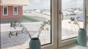 A window with two vases on the windowsill, a view of a marina with boats, a brick building, and a grassy area.