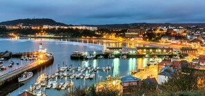 A harbor with boats docked, a lighthouse, and buildings along the waterfront.
