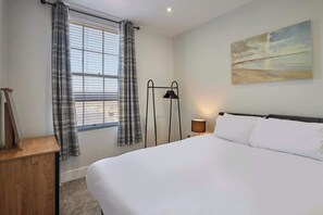 Une chambre d’hôtel avec un lit, une fenêtre avec des rideaux, une lampe et un tableau au mur.