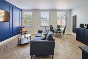 Una sala de estar moderna con un sofá, una mesa de vidrio y un televisor montado en la pared.