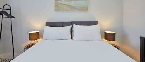 A neatly made bed with white linens, two bedside lamps, and a painting above the headboard.